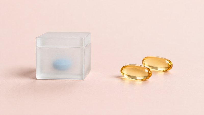 A tablet hidden in a frosted box next to two clear amber softgels